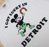 Close-up of cream colored t-shirt featuring a retro Mickey cartoon character holding a horseshoe with the text 'I Got Lucky in Detroit' in bold black letters