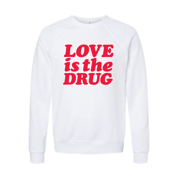 White crewneck sweatshirt with bold bright orangey red 'Love is the Drug' text across the chest