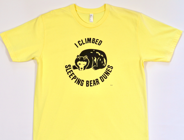 Graphic tee with a bear and 'I Climbed Sleeping Bear Dunes' text in black on a yellow shirt